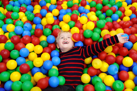 Happy little boy having fun in ball pit with colorful balls. Child playing on indoor playground. Kid...