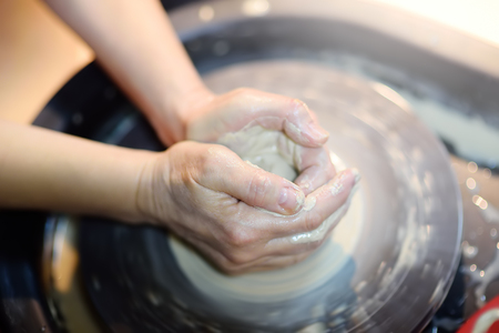 Close-up photo of hands of woman making clay object. Creating a jar or vase of white clay in pottery workshop. The sculptor during her work. Twisted potter's wheel.の写真素材