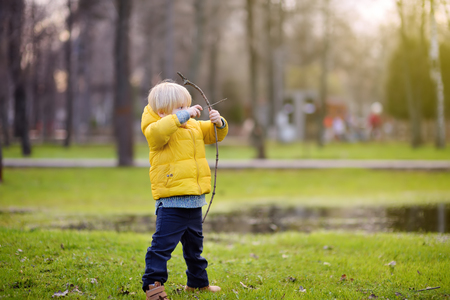 Little boy playing with sticks during stroll in the park at spring, summer or autumn day. Active family time on nature. Hiking with little kidsの写真素材