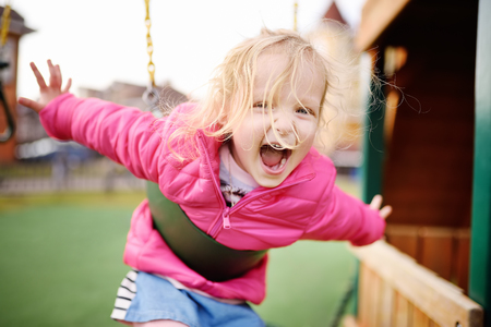 Cute little girl having fun on outdoor playground. Spring/summer/autumn active sport leisure for kids. Child on plastic swingの写真素材