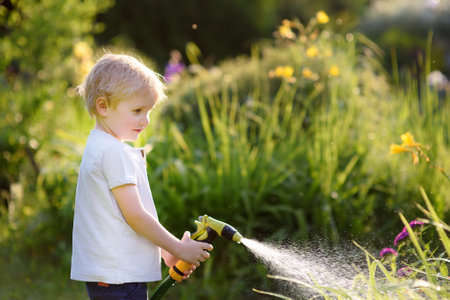 Funny little boy playing with garden hose in sunny backyard. Preschooler child having fun with spray of water. Summer outdoors activity for kids.のeditorial素材