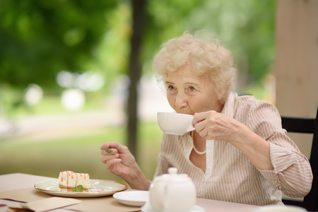 Beautiful senior lady with curly white hair drinking tea in outdoors cafe or restaurant. Elderly lady lifestyleの写真素材