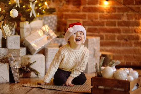 Cute little boy wearing Santa hat ready for celebrate holiday. Portrait of happy kid on Christmas eve. Cozy living room with decorated fir treeの写真素材