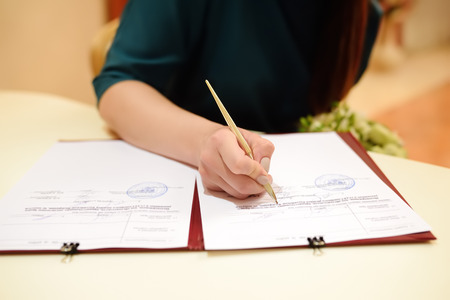 Bride signing marriage license or wedding contract during ceremony. Woman sign the...