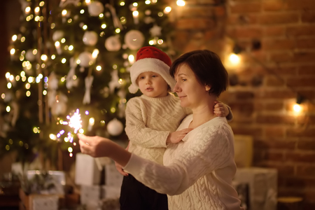 Mother or grandmother with her little son or grandson celebration Christmas with sparkler in cozy living room in winterの写真素材