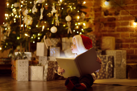 Little boy reading a magic book in decorated cozy living room. Portrait of happy kid on Christmas eve. Activity for children on winter holidaysの写真素材