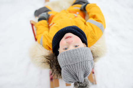 Little boy enjoying a sleigh ride in winter park. Outdoor winter activities for family with kids. Glad preshooler child sleddingの写真素材