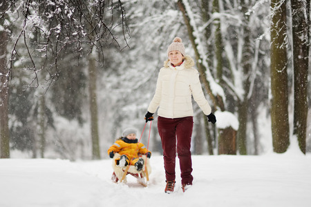 Little boy enjoying a sleigh ride. Mother/grandmother/nanny sled his cute child. Family winter...