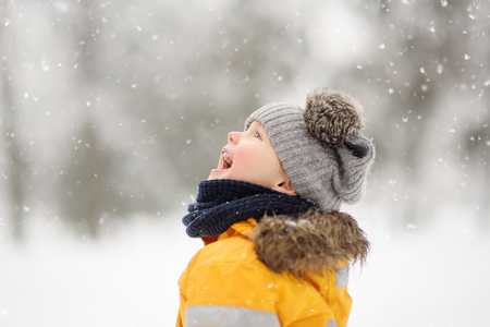 Cute little boy in yellow winter clothes walks during a snowfall. Outdoors winter activities for kids.の写真素材