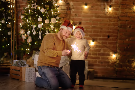 Father with her little son celebration Christmas with sparkler in cozy living room in winterの写真素材