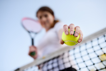 Young female tennis player with tennis ball and racket preparing to serve. Girl on tennis court. Focus on ball.の写真素材