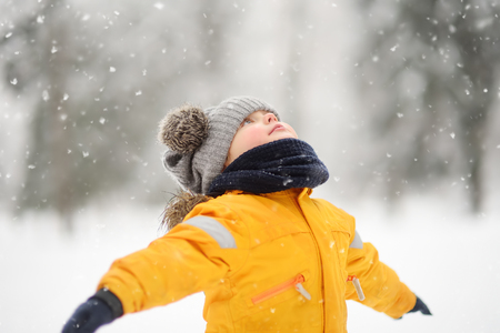 Cute little boy in yellow winter clothes walks during a snowfall. Outdoors winter activities for kids.の写真素材