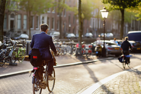 An elegantly dressed man rides a Bicycle in the center of Amsterdam. Bicycle capital of Europe.の写真素材