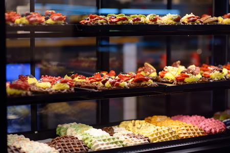 Belgian and Liege waffles with chocolate, berries, sweet sauce, cream in the window of cafe or shop. Sweets.の写真素材