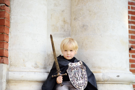 Portrait of a cute little boy dressed as a medieval knight with a sword and a shield. Medieval festival or costume party for kidsの写真素材
