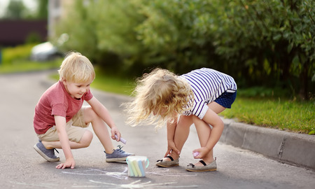 Happy little boy and girl drawing with colored chalk on asphalt. Creative leisure for toddler child. Street art, kids education.の写真素材