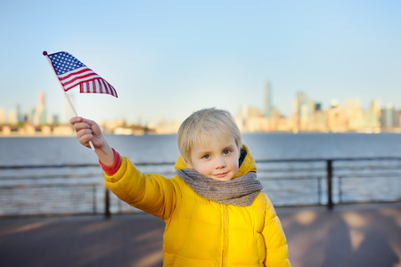 Little boy holding the American flag on the background skyscrapers of Manhattan. The concept of family travelの写真素材
