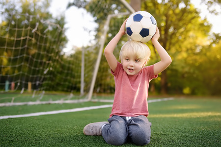Little boy having fun playing a soccer/football game on summer day. Active outdoors game/sport for children. Kids soccer classes and campsの写真素材