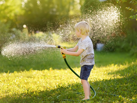 Funny little boy playing with garden hose in sunny backyard. Preschooler child having fun with spray of water. Summer outdoors activity for kids.の写真素材
