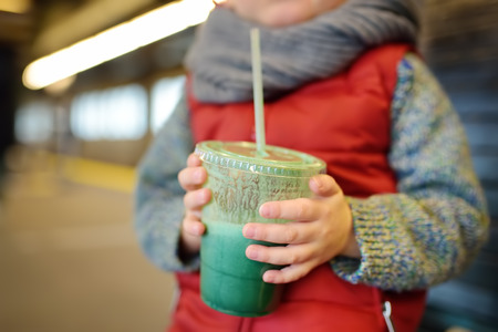 A little boy drinks a fresh fruit or vegetable smoothie. Healthy fastfood for kids in the city.