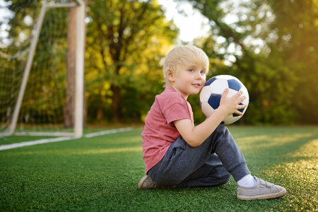 Little boy having fun playing a soccer/football game on summer day. Active outdoors game/sport for children. Kids soccer classes and campsの写真素材