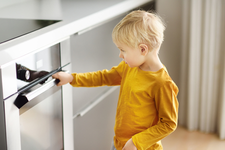 Charming boy waiting preparing food in domestic kitchen. Little mom's helper looks into oven and...