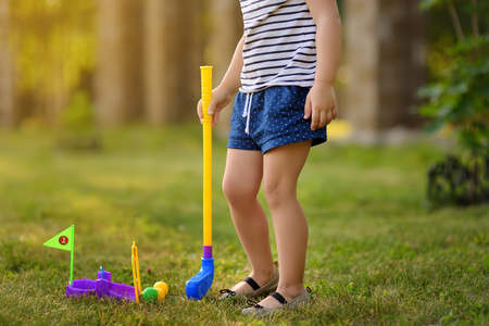 Little girl playing mini golf in spring park. Child having fun with active leisure on vacations. Baby on golf course.の写真素材