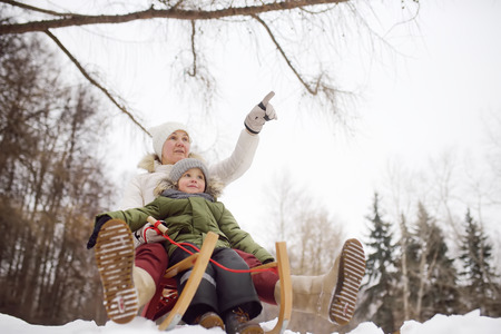 Little boy and mother/grandmother/nanny sliding in the Park. Outdoor winter activities for family with kids.の写真素材