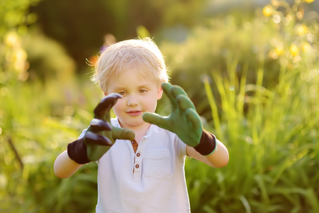 Funny little boy wearing garden gloves. Garden tools and gloves outdoors. Gardening activity with little kid and family.の写真素材