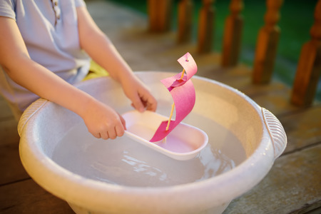 Cute little boy playing with homemade ship in basin of water on the porch of house. Kids play. Imagination.の写真素材