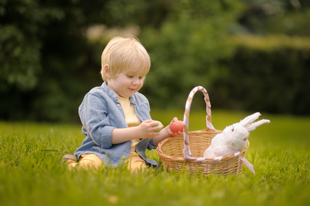 Charming little boy hunting for easter egg in spring park on Easter day. Cute little child with...