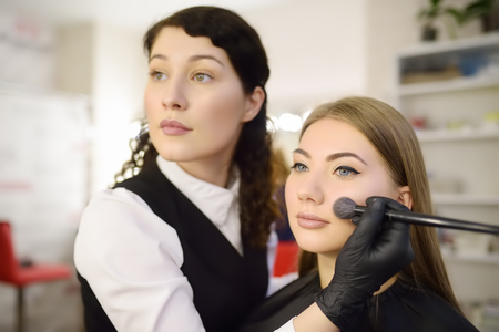Makeup artist applying the tone of the foundation using special brush on face young beautiful model. Facial care and make up. Professional beauty salonの写真素材