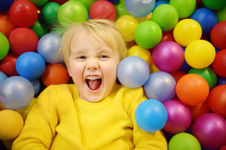 Happy little boy having fun in ball pit with colorful balls. Child playing on indoor playground. Kid jumping in ball pool.の写真素材