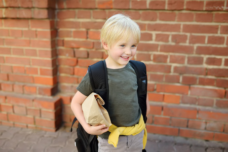 Student with big backpack and lunch bag near the school building. Back to school
