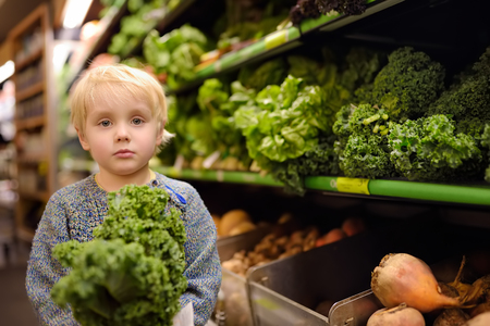 Cute toddler boy in a food store or a supermarket choosing fresh organic kale salad. Healthy lifestyle for young family with kidsの写真素材