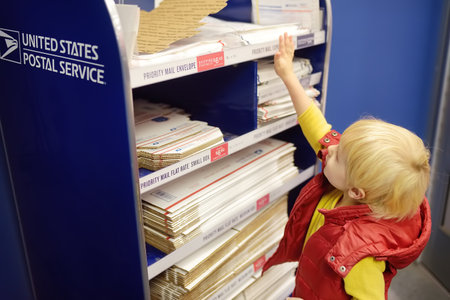 NEW YORK, USA - 23 OCTOBER 2018: Little boy at the post office chooses an packaging - envelope or...