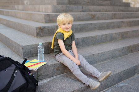 Little student sitting on staircase near the school building. Back to school. Education.の写真素材