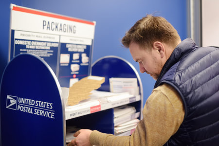 NEW YORK, USA - 23 OCTOBER 2018: Mature man at the post office chooses an packaging - envelope or box for mailing. Postal system of the United Statesのeditorial素材