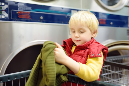 Little boy loads clothes into the drying machine in public laundrette. Mommy's helper in laundryの写真素材