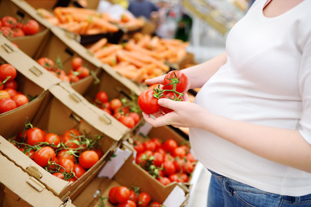 Pregnant woman in a food store or a supermarket choosing fresh organic tomatoes. Healthy eating for expectant motherの写真素材