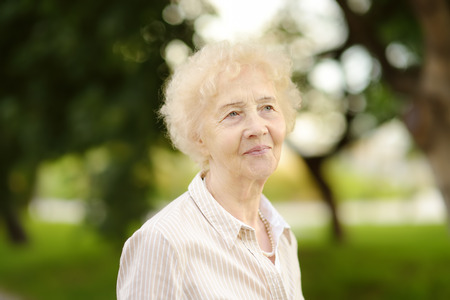 Outdoor portrait of beautiful senior woman with curly white hair. Elderly lady in parkの写真素材