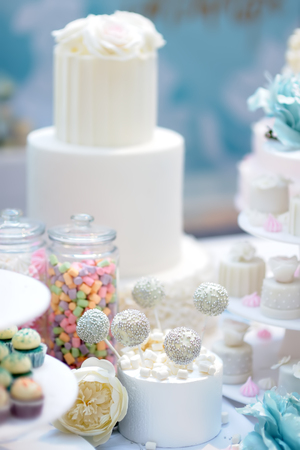Traditional anniversary/wedding multi-layer cake decorated with flowers. And beautiful delicious sweet dessert - cupcakes, marshmallow, vanilla cake pops on blurred backgroundの写真素材