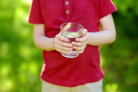Little boy drinking glass of water in hot sunny summer day on the backyard or home garden. Healthy lifestyle for children.の写真素材
