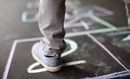 Closeup of little boy's legs and hopscotch drawn on asphalt. Child playing hopscotch game on...
