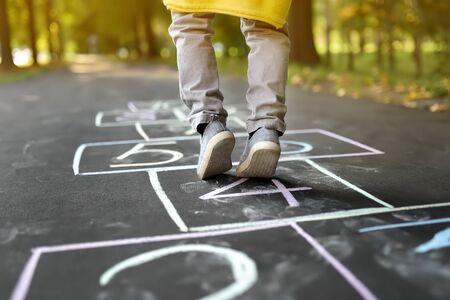 Closeup of little boy's legs and hopscotch drawn on asphalt. Child playing hopscotch game on playground outdoors on a sunny day. Summer activities for children.の写真素材