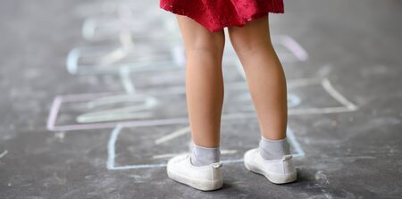 Closeup of little girl's legs and hopscotch drawn on asphalt. Child playing hopscotch game on...