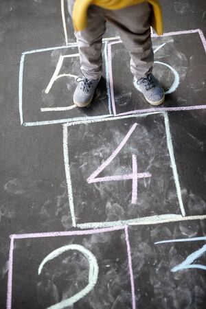 Closeup of little boy's legs and hopscotch drawn on asphalt. Child playing hopscotch game on playground outdoors on a sunny day. Summer activities for children.の写真素材