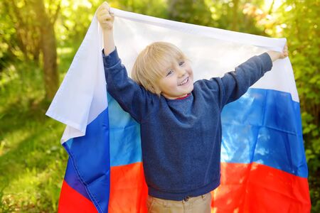 Portrait of cute little boy in public summer park with russian flag on background. Fans child supporting and cheering their national team. Day of independence. Pride and patriotism.の写真素材