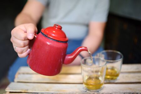 Man pours tea from kettle into cups at table in cafe of Israeli cuisine. Traditional Israeli beverage.の写真素材