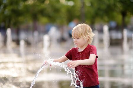 Little boy plays in the square between the water jets in the fountain at sunny summer day. Active summer leisure for kids in the city.の写真素材